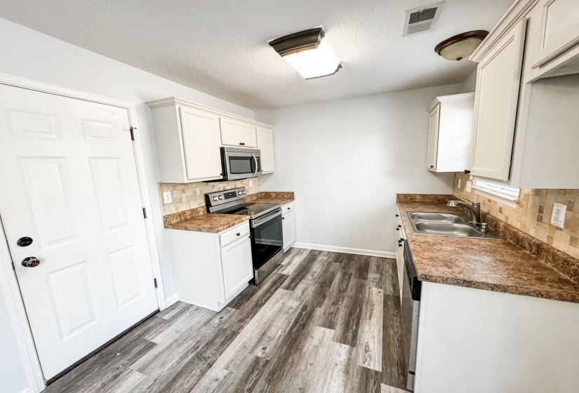 Kitchen featuring appliances with stainless steel finishes, dark wood-style floors, backsplash, a textured ceiling, and white cabinets