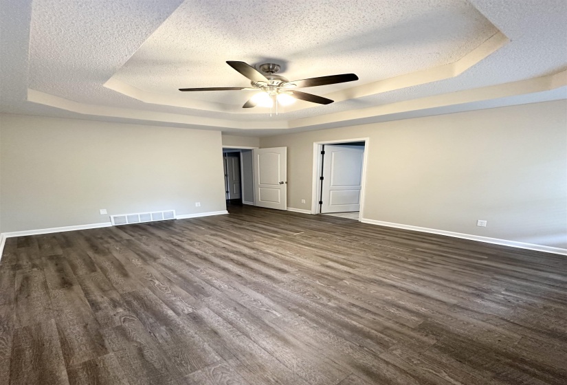 Spacious room featuring a tray ceiling with a ceiling fan, light gray wall paint, and wood-finish flooring