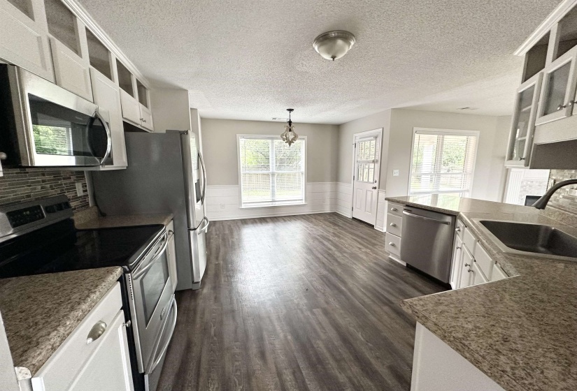 Kitchen and dining area featuring wood-finish flooring, white cabinetry, granite-style countertops, stainless steel appliances, and a mosaic tile backsplash