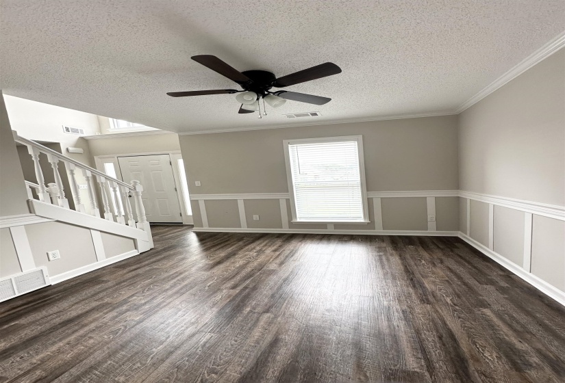 Spacious room featuring wood-finish flooring, a ceiling fan with integrated lighting, crown molding, and wainscoting