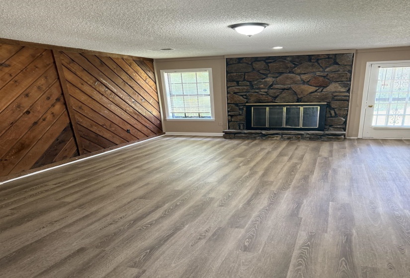 Spacious interior featuring wide-plank wood-finish flooring, a stone fireplace with a black metal enclosure, and a distinctive diagonal wood-paneled accent wall