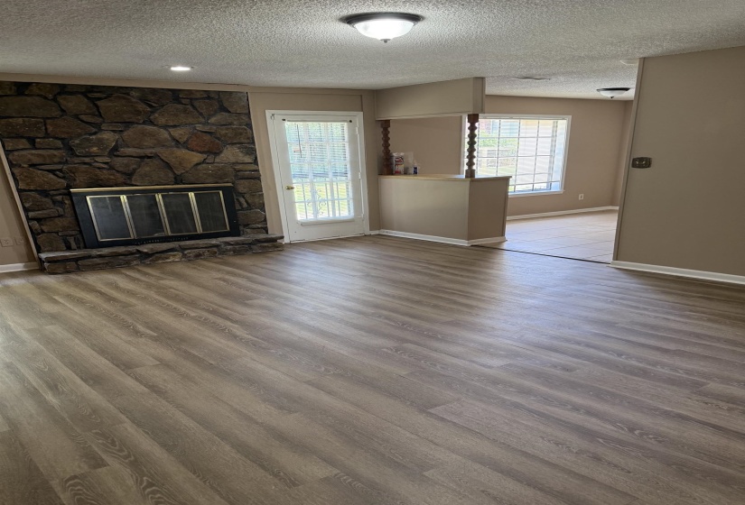 Spacious living area featuring wood-finish flooring, a stone fireplace with a black metal screen, and a ceiling-mounted light fixture