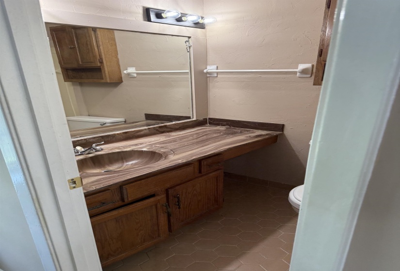 Bathroom vanity featuring a patterned countertop with integrated sink, oak-finish cabinetry, and hexagonal floor tiling