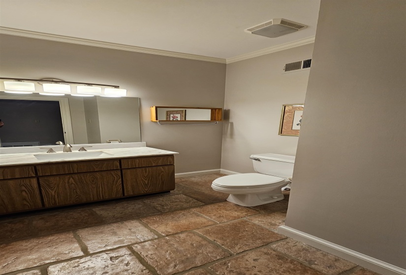 Bathroom featuring large format stone tile flooring, a wood-finish vanity with a white countertop and double sinks, and crown molding