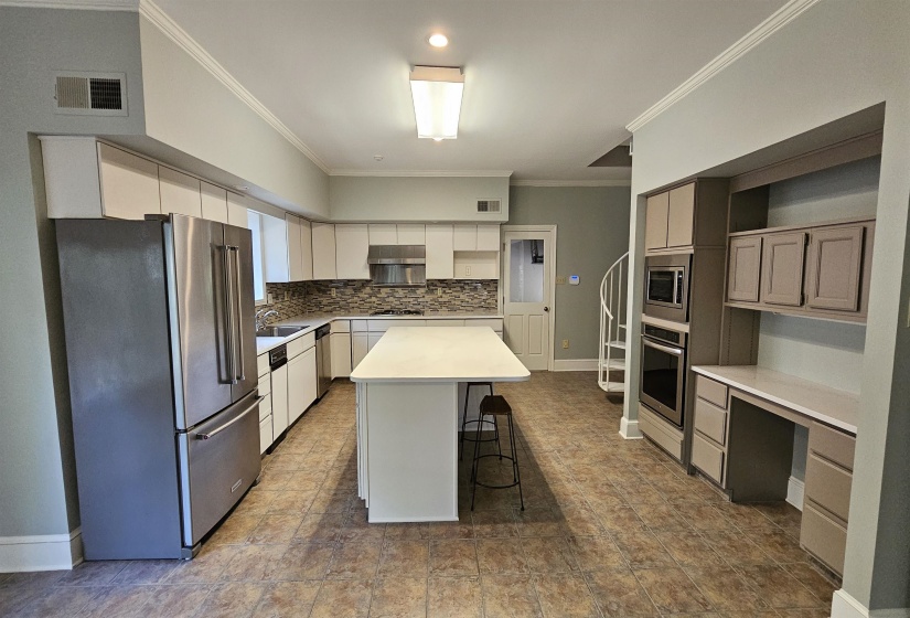Spacious kitchen featuring an expansive center island, extensive white cabinetry, stainless steel appliances, and a tiled backsplash