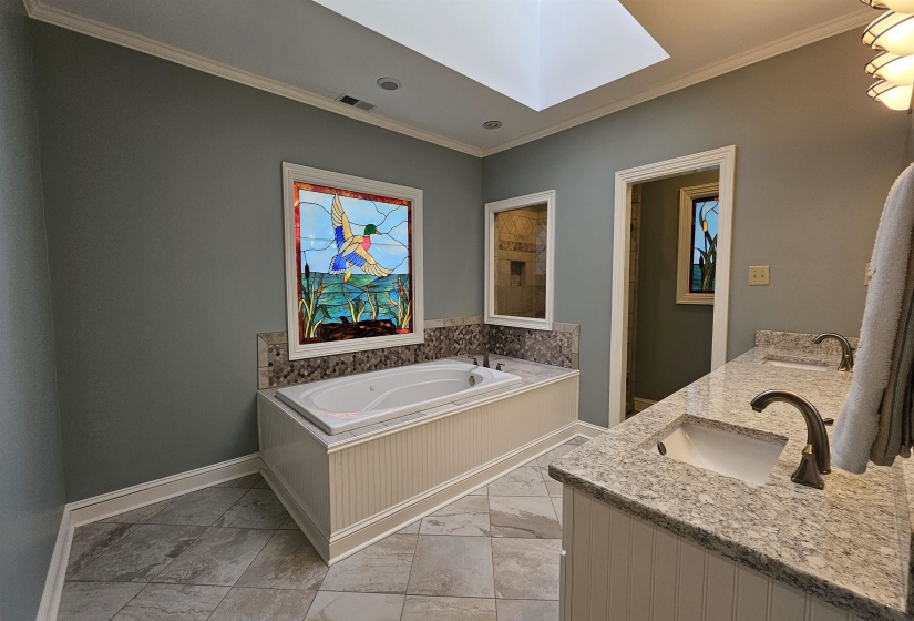 Spacious bathroom featuring a built-in jetted tub with beadboard paneling, surrounded by a mosaic tile backsplash and granite countertop
