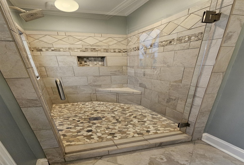 Walk-in shower featuring pebble stone floor, built-in corner bench, recessed niche, and decorative tile accents