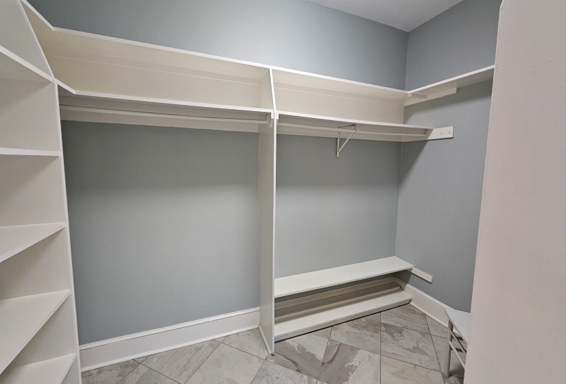Walk-in closet featuring built-in white shelving, hanging rods, and a tiled floor