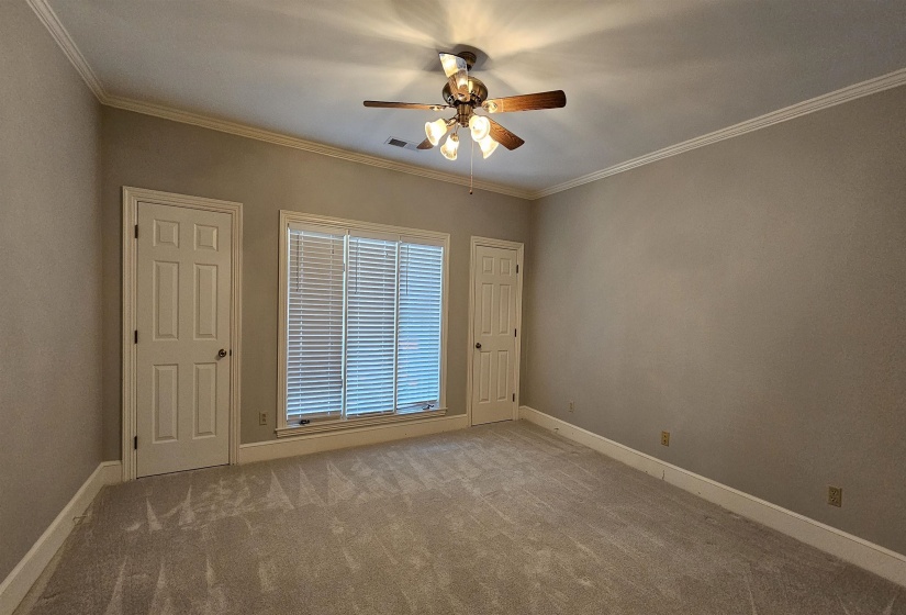 Spacious room featuring neutral carpeting, a multi-pane window with blinds, two paneled doors, crown molding, and a ceiling fan with integrated lighting