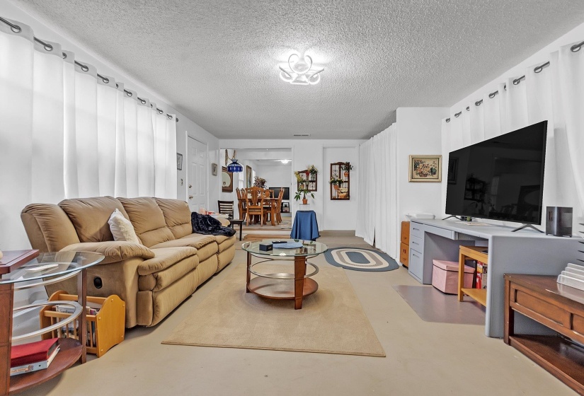 Spacious living area featuring light-colored flooring, white walls, and a textured ceiling