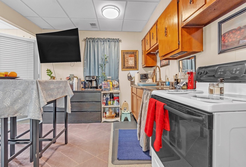 Compact kitchen featuring wood-finish cabinetry, a white electric range, and a drop-in sink with a gooseneck faucet