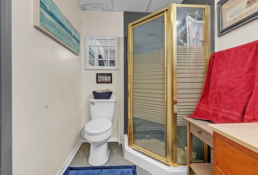 Compact bathroom featuring a corner shower with gold-tone framing and frosted glass panels