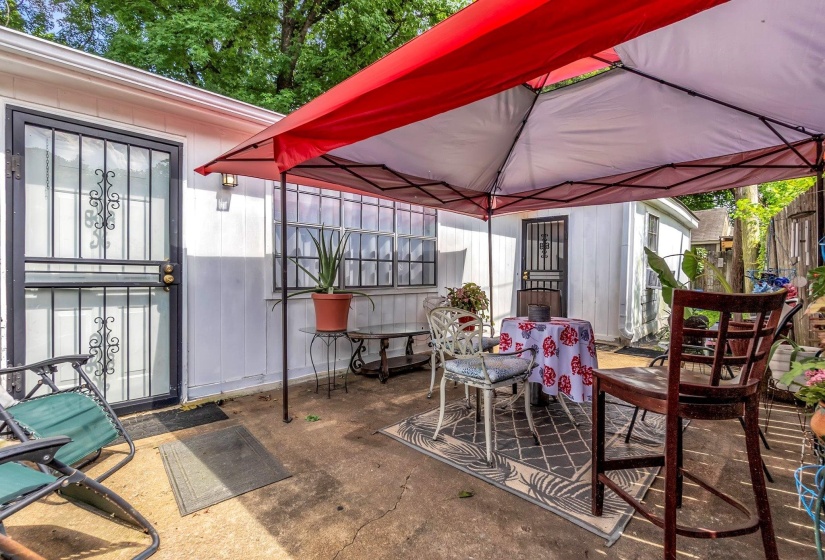 Concrete patio area featuring a white exterior wall, exterior door with security screen, and a window with security bars