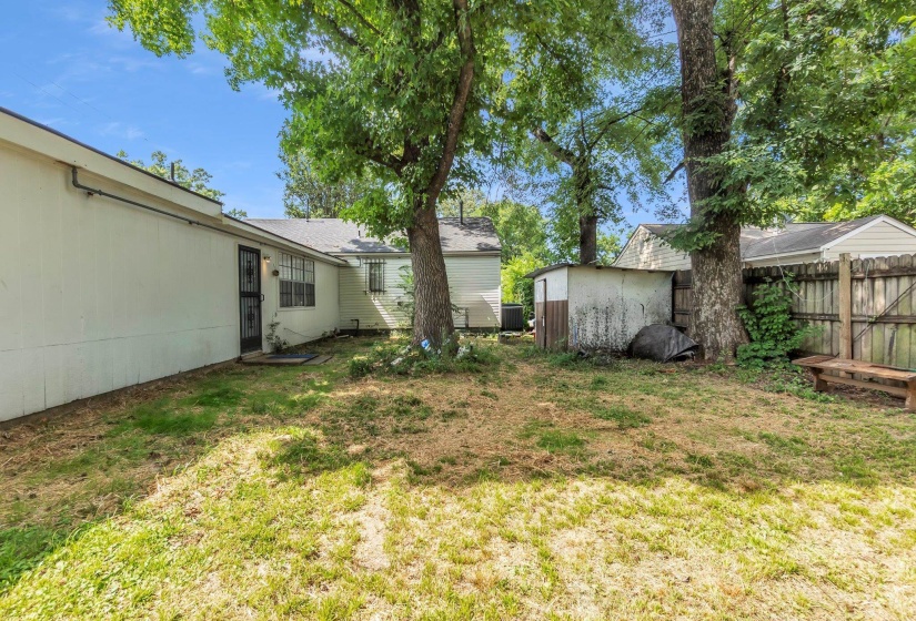 Expansive exterior featuring mature trees, a privacy fence, a detached shed, a white siding facade, and a security screen door