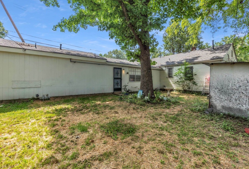 Expansive rear yard featuring mature trees, a detached storage structure, and a security screen door entry