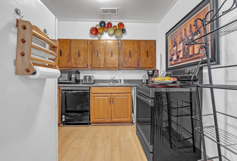 Kitchen featuring wood-finish flooring, a stainless steel sink, black appliances, and wood cabinetry