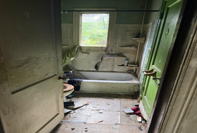 Bathroom featuring a single window, a built-in bathtub, a toilet, and tiled flooring
