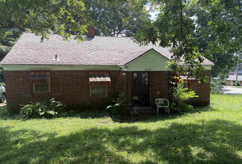 Brick exterior featuring a gabled entry, asphalt shingle roof, and two front windows with decorative awnings