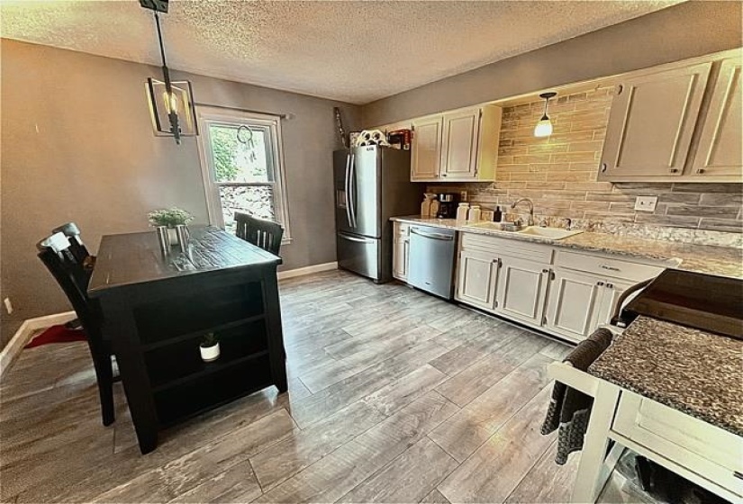 Kitchen with decorative backsplash, pendant lighting, sink, appliances with stainless steel finishes, and light hardwood / wood-style flooring