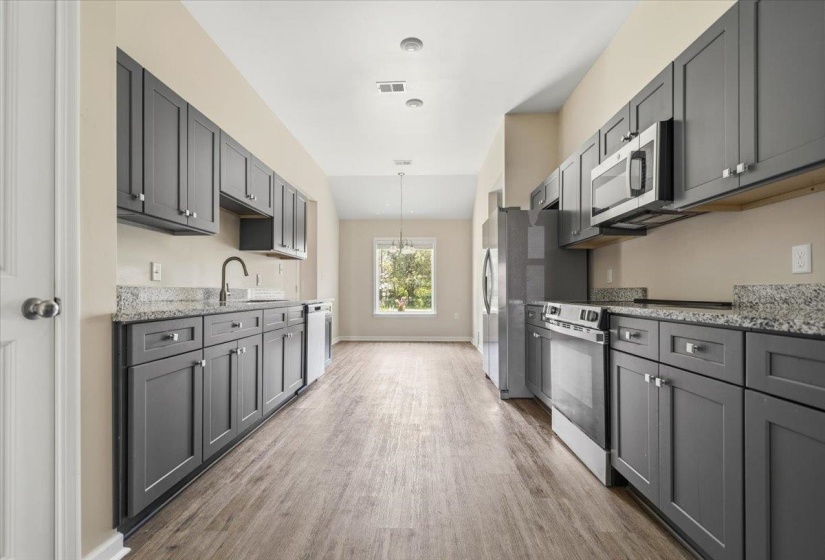 Galley kitchen featuring gray cabinetry, light granite countertops, stainless steel appliances, wood-finish flooring, and a window with outdoor scenery