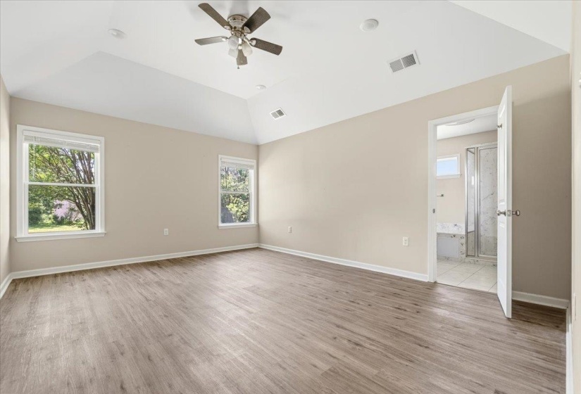 Spacious room featuring vaulted ceilings, wood-finish flooring, two windows with white blinds, a ceiling fan, and a neutral color palette