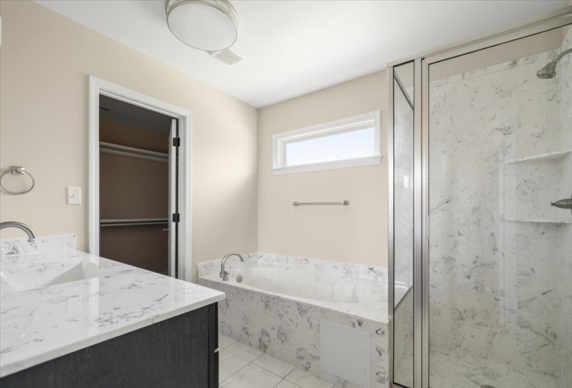 Bathroom featuring a dual vanity with white countertops, a built-in bathtub with a white surround, and a glass-enclosed shower with white-patterned wall panels and an integrated niche
