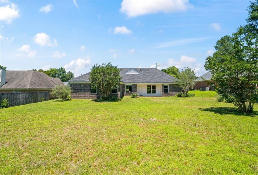 Spacious backyard with a lush green lawn, mature trees, and a brick exterior home featuring multiple windows