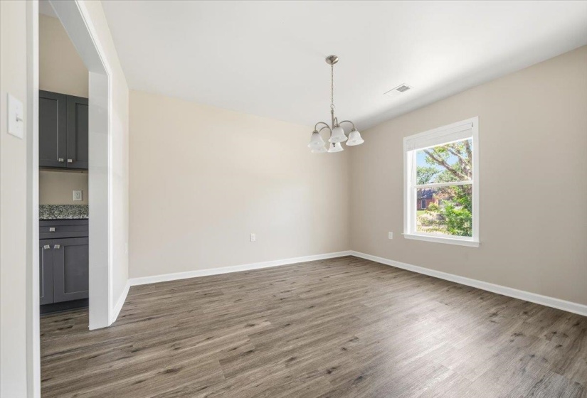 Spacious room featuring wood-finish flooring, a contemporary chandelier, and ample natural light from the large window