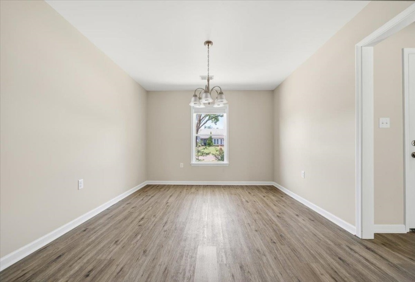 Spacious room featuring wood-finish flooring, neutral paint, a single window, and an overhead chandelier with frosted glass shades