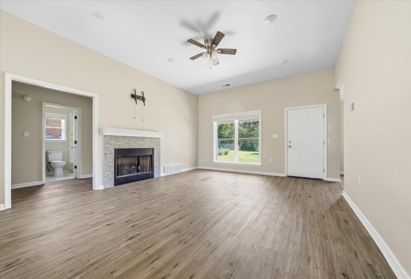 Spacious living area featuring wood-finish flooring, a tiled fireplace with a white mantel, and a vaulted ceiling with a ceiling fan