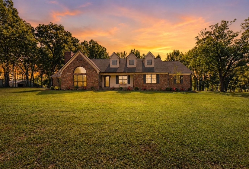 Beautiful brick home showcased at sunset, highlighting its timeless architecture, inviting front porch, and picturesque setting on approximately 13 private acres.