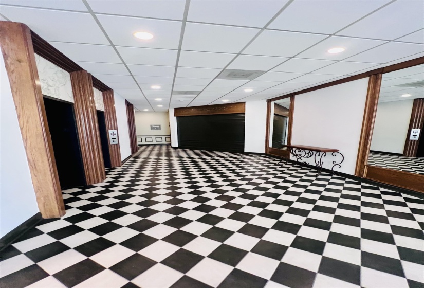 Hallway featuring black and white checkered flooring, recessed ceiling lights, paneled wood trim, and elevator access