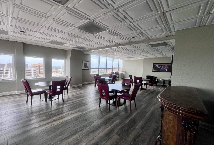 Spacious room featuring wood-finish flooring, patterned ceiling panels, and multiple large windows