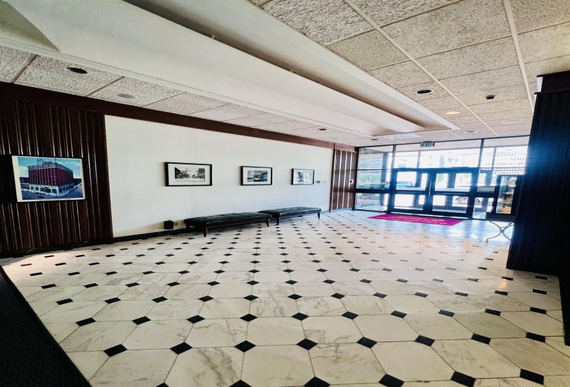Spacious entry lobby featuring patterned tile flooring, wood paneling, recessed lighting, and a glass-paneled entrance