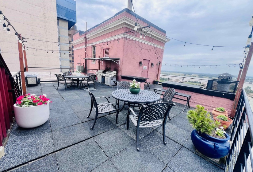 Expansive rooftop terrace with dark paver flooring, string lighting, and metal railings
