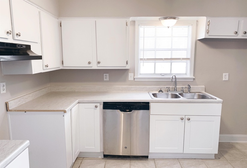 Kitchen with dishwasher, light countertops, white cabinets, and light tile patterned floors