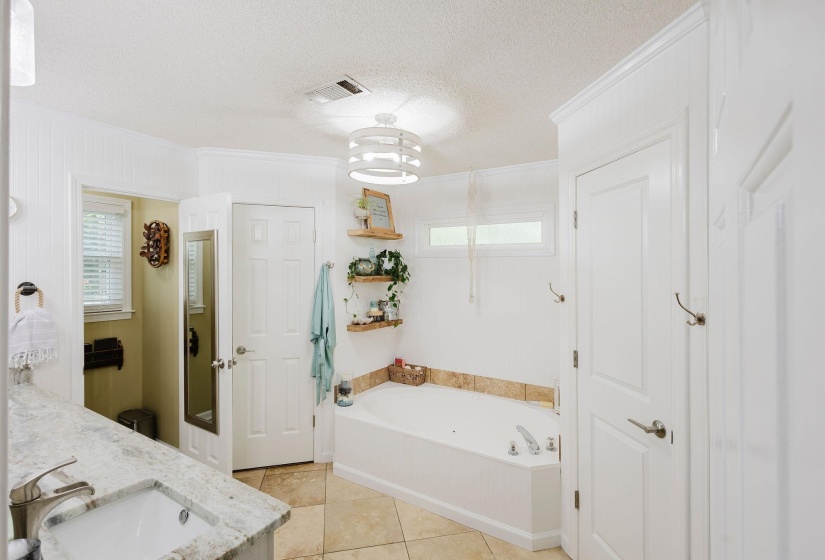 Bathroom featuring a built-in tub, a vanity with an undermount sink and stone countertop, tile flooring, and white paneling