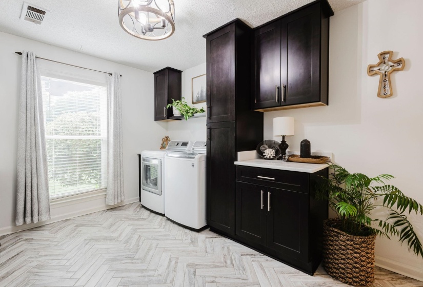 Laundry room featuring wood-finish herringbone flooring, dark cabinetry with brushed nickel hardware, and a white countertop