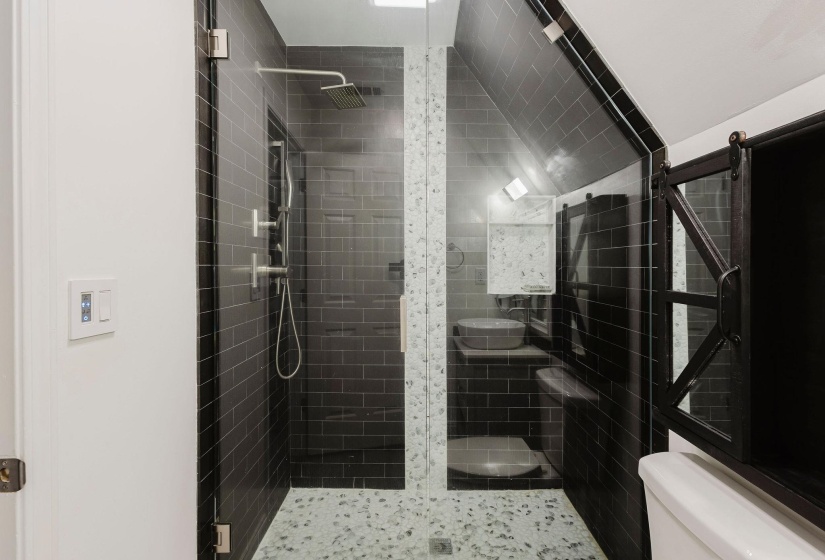 Walk-in shower featuring a rain showerhead, handheld shower fixture, and pebble-finish floor