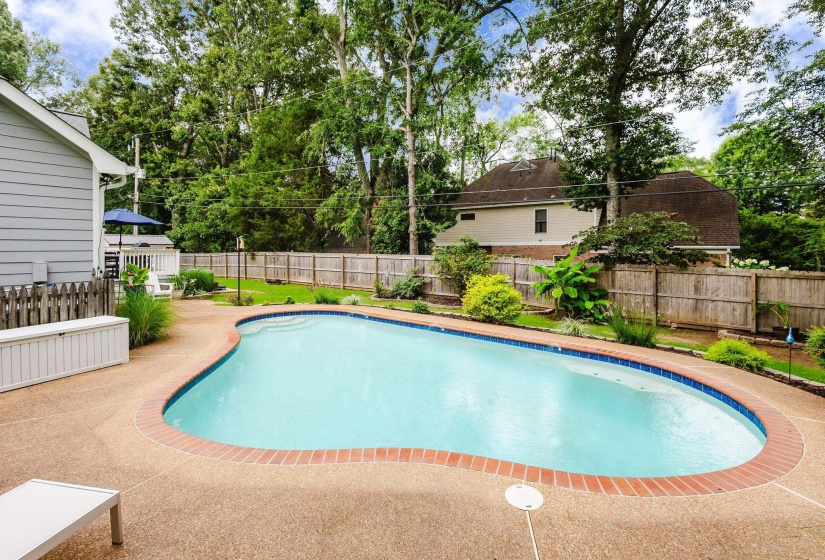Freeform swimming pool with integrated steps, brick coping, and a surrounding aggregate concrete deck