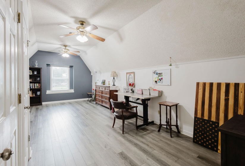 Spacious room featuring vaulted ceilings, wood-finish flooring, and multiple ceiling fans