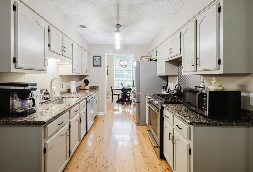 Galley kitchen featuring light wood-finish flooring, white cabinetry, dark speckled countertops, and a stainless steel refrigerator