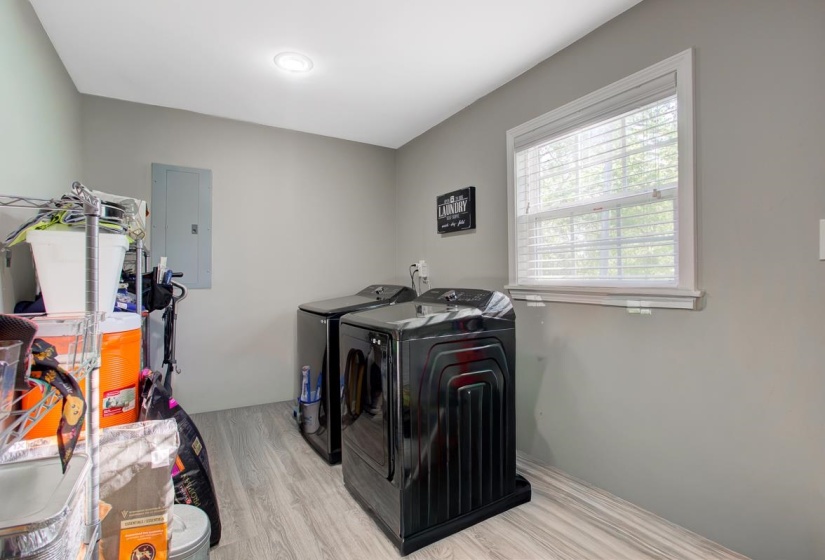 Laundry area with electric panel, light LVP flooring, and washer and dryer