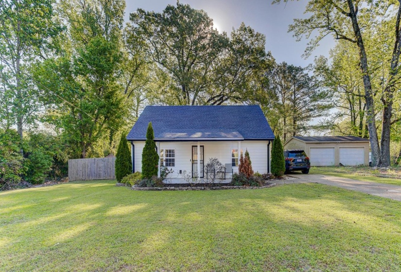 View of front of property with covered porch, roof with shingles, and view of wooded area. Detached garage is NOT part of this property, belongs to home next door.