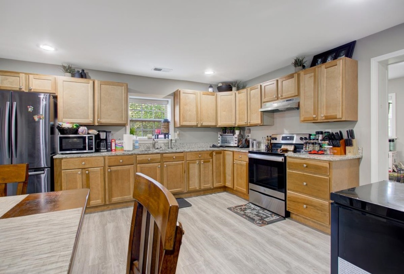 Kitchen with stainless steel appliances, light stone countertops, light LVP flooring, recessed lighting, and light wood finish cabinetry