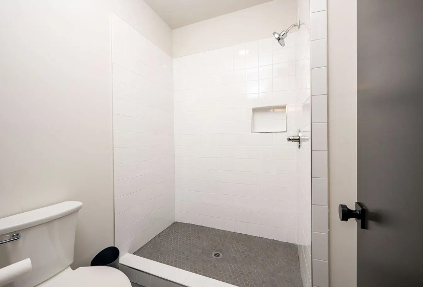 Walk-in shower featuring white subway tile surround, integrated shower niche, and a grey hexagon tile floor