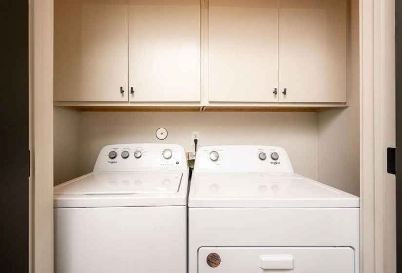 Dedicated laundry area featuring overhead cabinetry with dark hardware and a wood-finish shelf