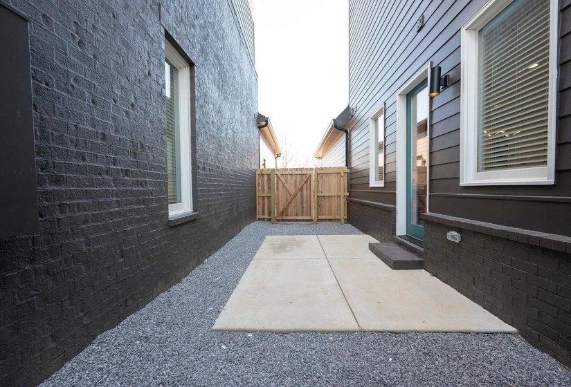 Private side patio featuring concrete paving, gravel landscaping, and a wooden privacy fence with gate