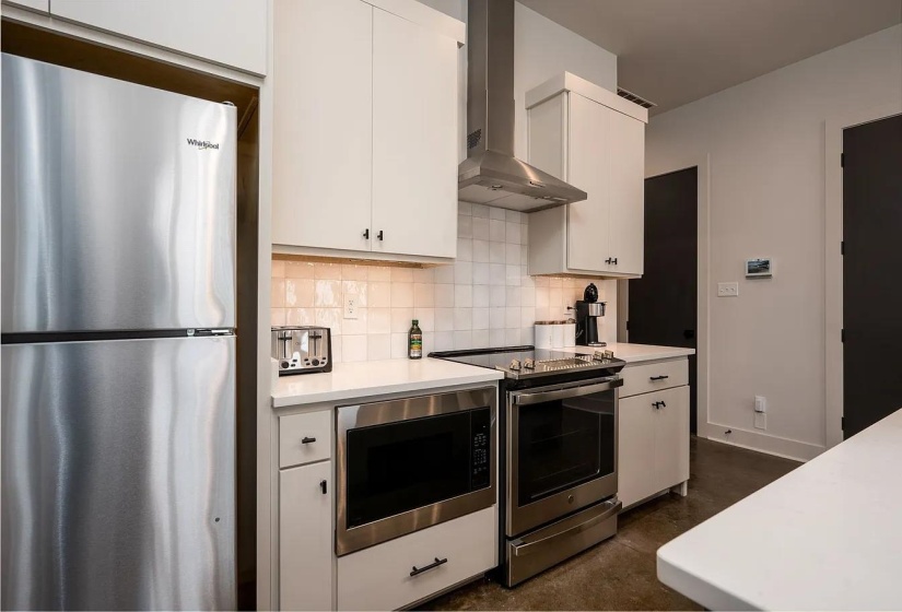 Modern kitchen featuring stainless steel appliances, white cabinetry, a square tile backsplash, and white countertops