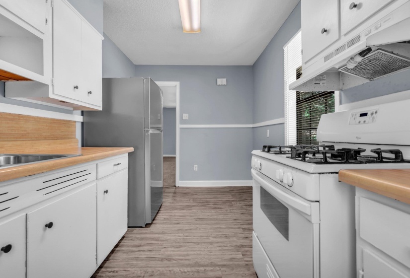 Kitchen featuring wood-finish flooring, white cabinetry, wood-look countertops, stainless steel refrigerator, and white gas range